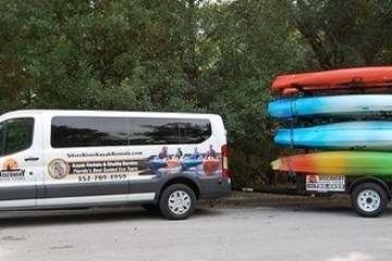 Van with logo towing a trailer carrying four stacked kayaks.