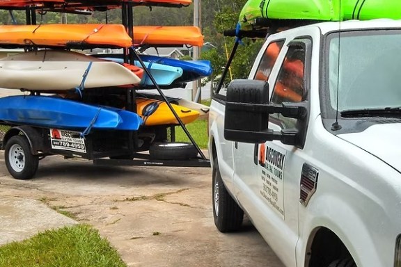 Truck with trailer carrying colorful kayaks on a residential driveway.